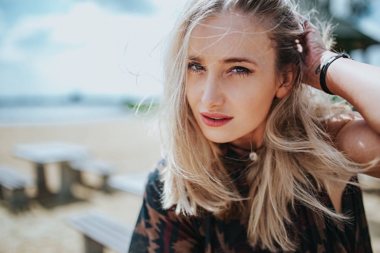 Beautiful blonde woman relaxing with a can of coke on a tree stump by the beach